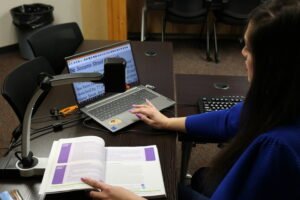 A woman using a MagniLink Magnifier to enlarge text in a textbook on a laptop screen.