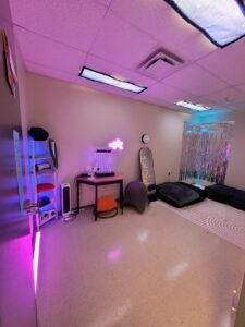 A sensory room at the Munsee Campus with florescent light covers, bean bag chairs, soft colourful lighting, a bubble tube, a rug and other sensory toys.