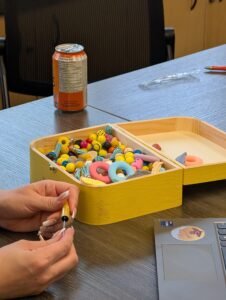 A yellow box filled with sensory beads with a set of hands making a sensory pen.