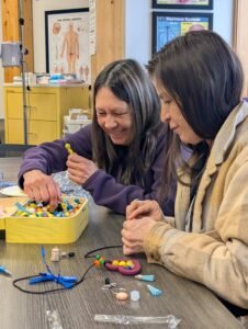 An older woman with a younger woman making sensory pens together gathering supplies from a box of sensory beads.